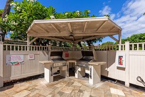 Un espace barbecue extérieur doté d’un coin grill couvert et d’une poubelle.