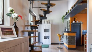 A modern kitchen with a central island, wooden staircase, and a dining area with a yellow chair. - Cipresso by Interhome (Lago di Vico)