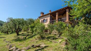Una casa con facciata in pietra, un balcone e vegetazione circostante.