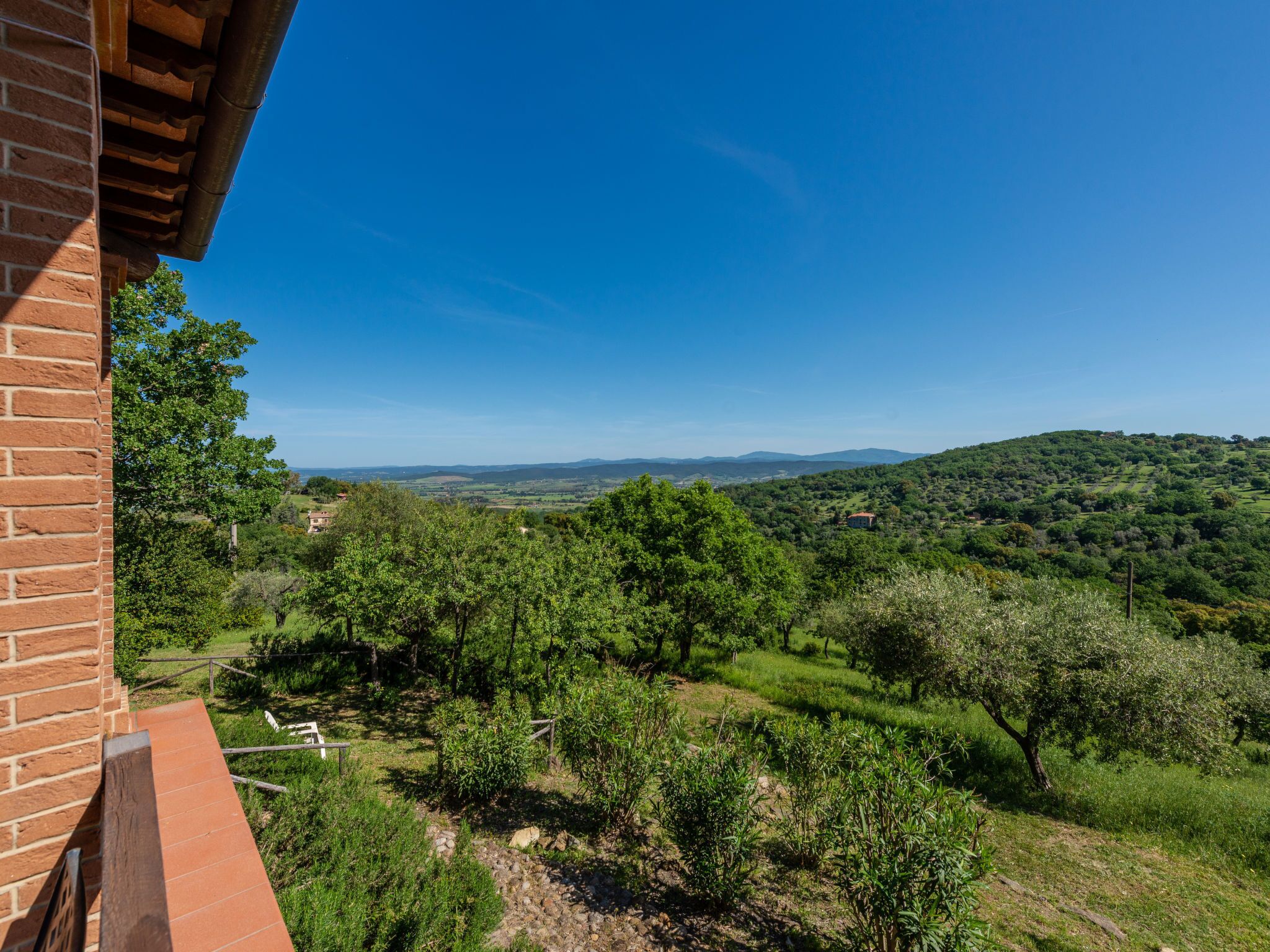 Un balcone con vista su un paesaggio verdeggiante, tra alberi e dolci colline all'orizzonte.