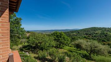 Un balcone con vista su un paesaggio verdeggiante, tra alberi e dolci colline all'orizzonte.