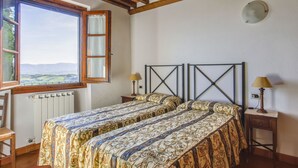 Ein Schlafzimmer mit zwei Betten, einem Fenster mit Blick auf die Landschaft, Holzbalken an der Decke und einer Heizung.