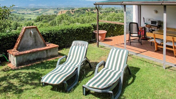 Eine Terrasse mit zwei gestreiften Liegestühlen, einem Grill und einem Tisch mit Stühlen.