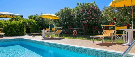 A swimming pool with tiled edges, surrounded by lounge chairs and yellow umbrellas.