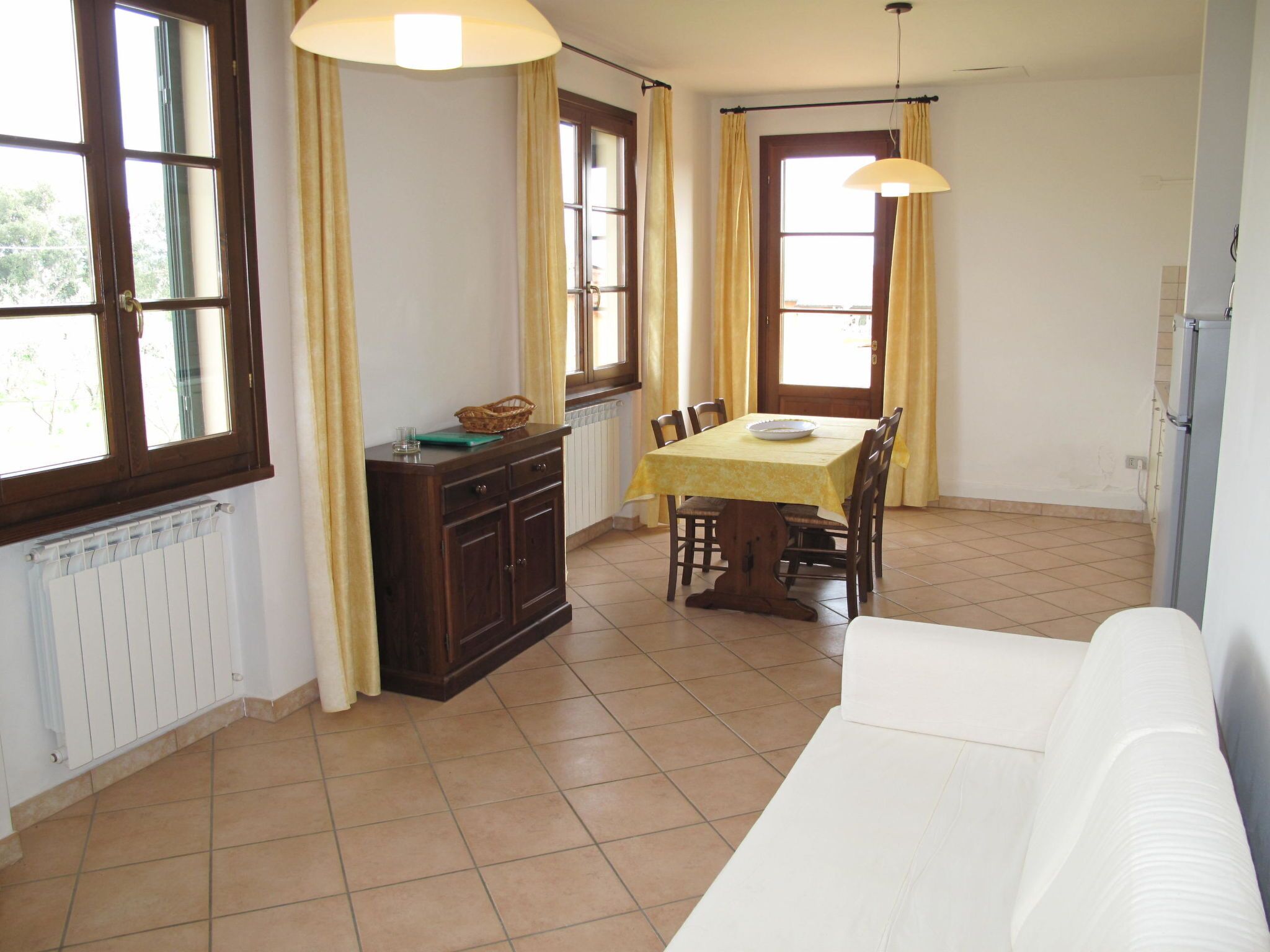 Un comedor con una mesa dispuesta para cuatro personas, un sofá blanco y una ventana con cortinas.