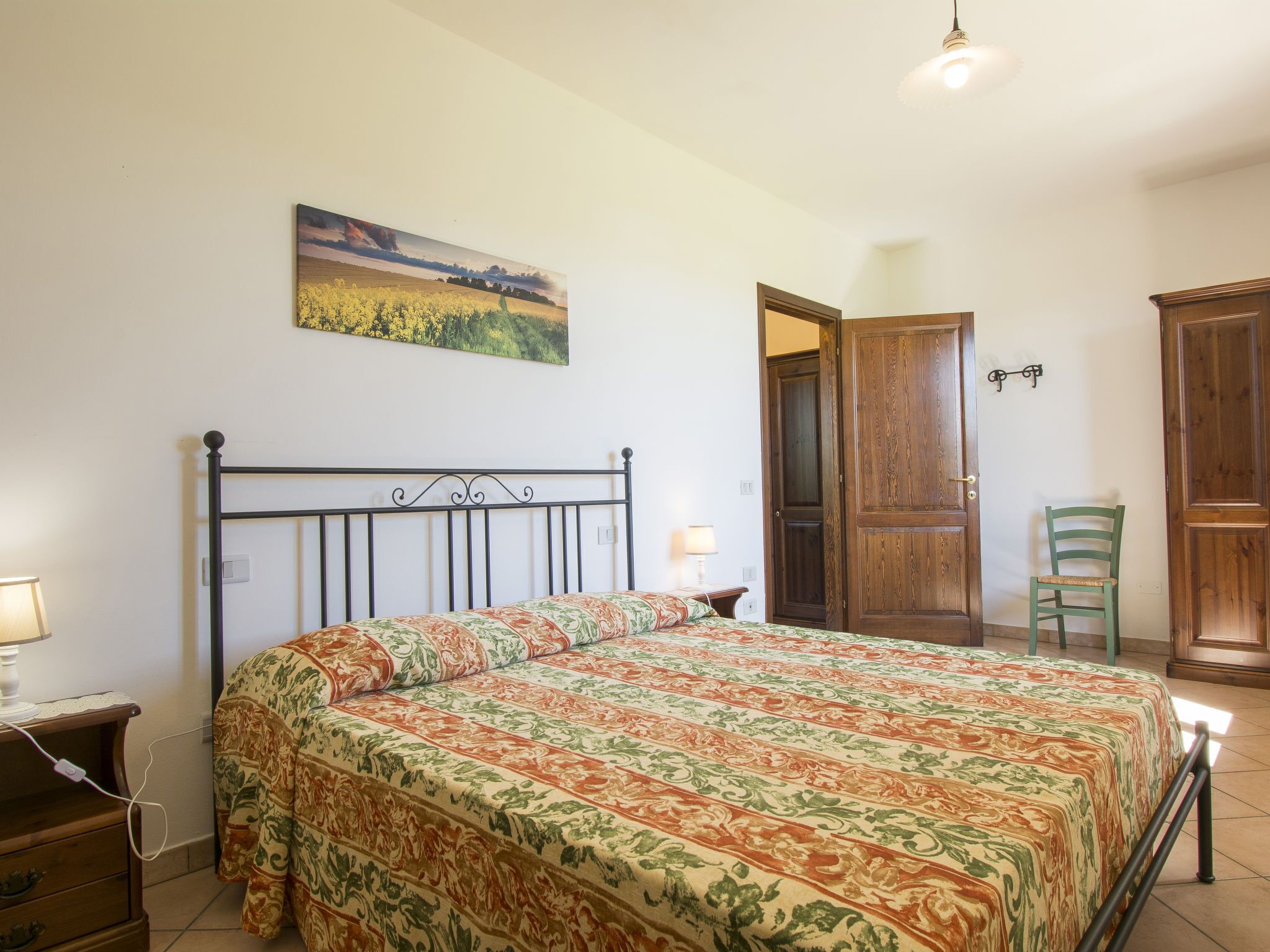 A bedroom with a bed, a nightstand, a lamp, a chair, and a door.