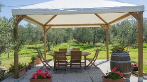 Un espace extérieur abrité, aménagé avec une table et des chaises, entouré de plantes en pot et d’un grand tonneau.