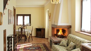 Un salon chaleureux avec une cheminée, un canapé, une table à manger avec des chaises et un tapis à motifs.