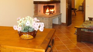 Un salon avec une cheminée, une table en bois ornée d’un vase de fleurs et un canapé à motifs.