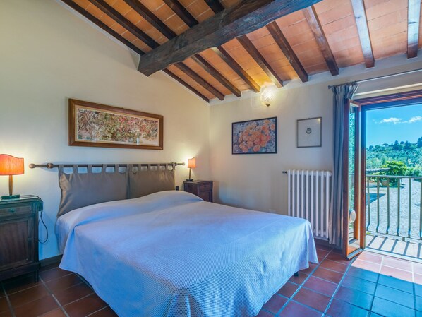 A bedroom with a bed, two bedside tables, a radiator, and a balcony with a view of greenery.
