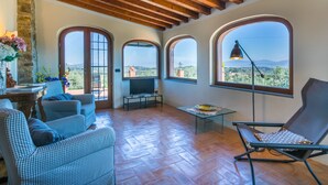 Amplia sala de estar con techo alto, vigas de madera y ventanas arqueadas que dan vistas al campo.