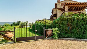 A villa with a stone facade, a wooden pergola, and a well-maintained garden with a gravel path and a metal gate. - Appartamento Ginepro - Borgo in Chianni by Interhome (Chianni)