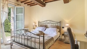 A bedroom with a metal bed frame, two bedside tables with lamps, a chair, and a stone wall. - Appartamento Ginepro - Borgo in Chianni by Interhome (Chianni)