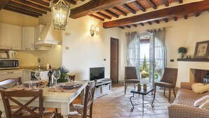 A cozy dining area with a wooden table, chairs, and a chandelier. There is a television and a window with curtains. - Appartamento Ginepro - Borgo in Chianni by Interhome (Chianni)
