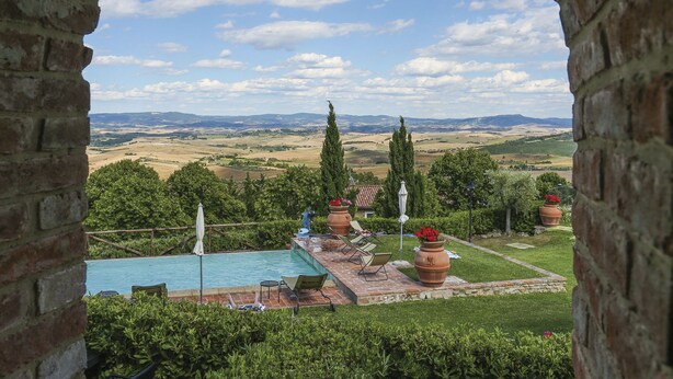 A view through a stone archway of a pool area with lounge chairs and potted plants, overlooking a scenic landscape with rolling hills and a clear sky. - Appartamento Ginepro - Borgo in Chianni by Interhome (Chianni)