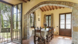 Comedor con arco de piedra, vigas de madera, suelo de baldosas y una mesa dispuesta para seis.