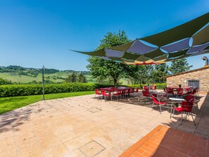 An outdoor patio with red chairs and tables, a stone building, and a view of green fields and hills.
