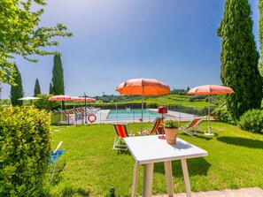 Un espace aménagé au bord de la piscine, avec plusieurs parasols, des chaises longues et une table agrémentée d’une plante en pot.