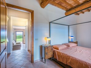 Relax in this serene bedroom with a four-poster bed and balcony overlooking a lush landscape.