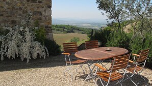 Un muro de piedra, una mesa redonda de madera con sillas de metal y vistas al paisaje campestre.