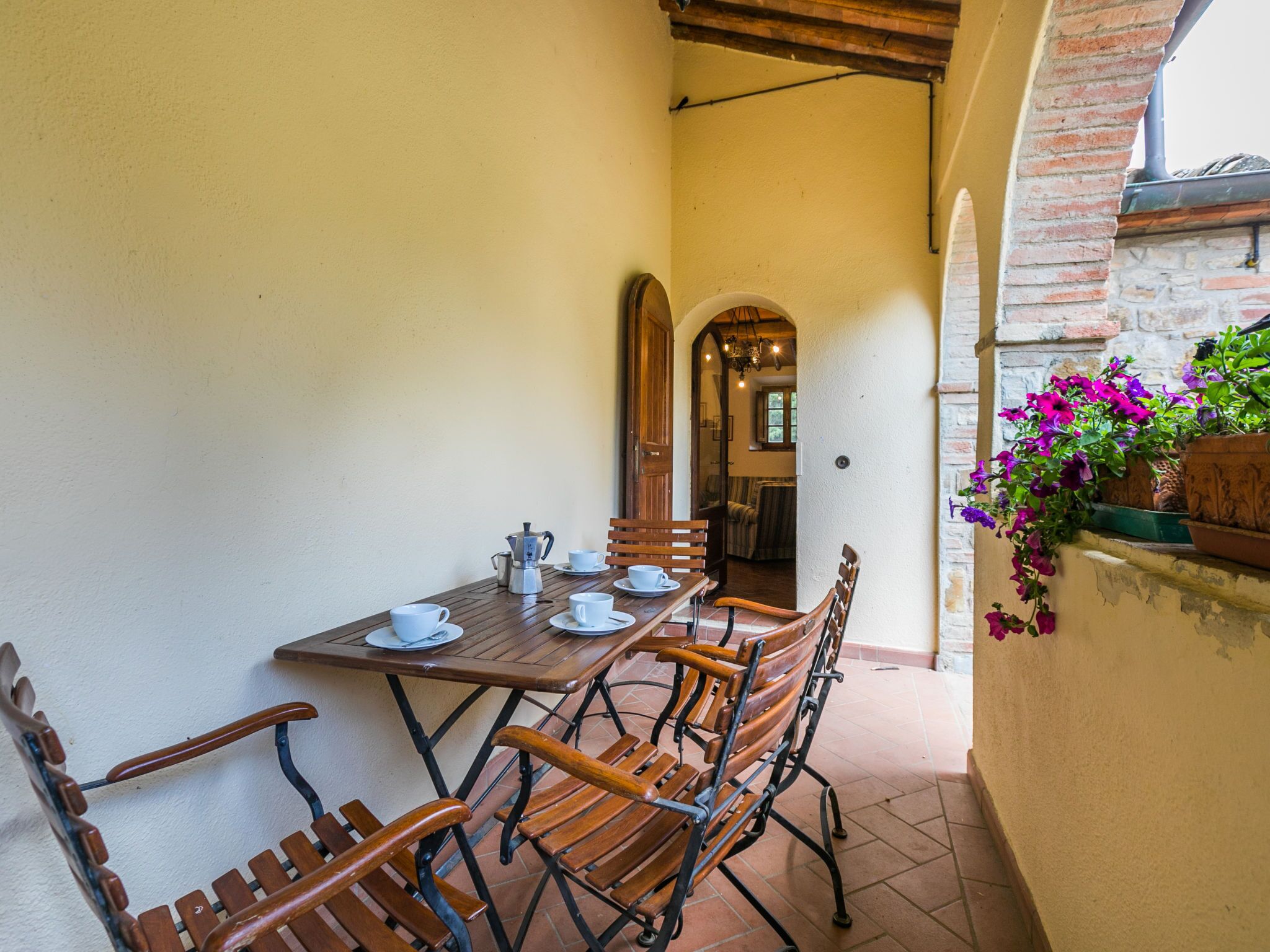 A dining area with a wooden table and chairs, a coffee pot, and a potted plant with purple flowers.
