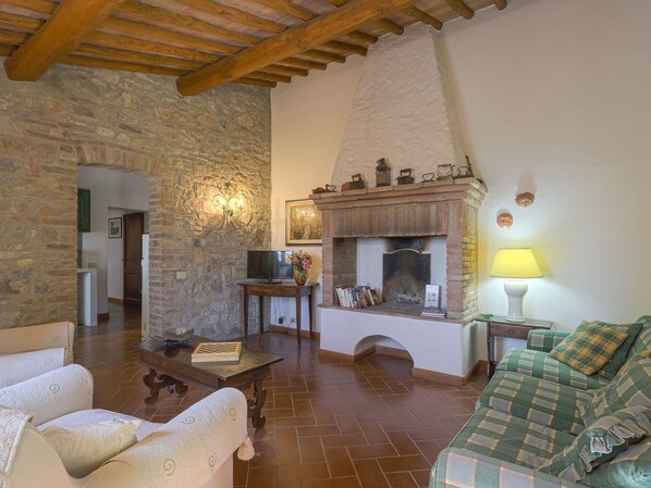 A cozy living room with a stone wall, a fireplace, a television, and a sofa. - Cellole - Cellole 2 (CTC151) by Interhome (Castellina in Chianti)