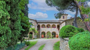 A courtyard with a gravel path leading to a stone building with arched walkways and a tower. - Cellole - Cellole 1 (CTC150) by Interhome (Castellina in Chianti)