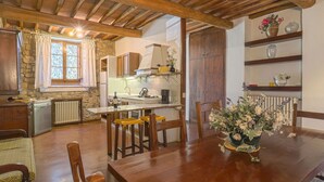 A rustic kitchen with wooden beams, a stone wall, and a dining area with a wooden table and chairs. - Cellole - Cellole 1 (CTC150) by Interhome (Castellina in Chianti)
