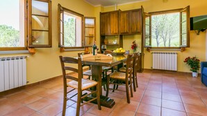 A kitchen with wooden cabinets, a dining table with chairs, and a TV mounted on the wall.