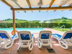 Un espace aménagé au bord de la piscine, avec des chaises longues et des parasols, offrant une vue dégagée sur la piscine, et un jardin paysager en arrière-plan.