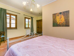 A bedroom with a large bed, a painting on the wall, and a view of the outside.