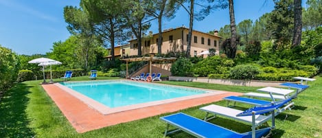 A swimming pool with blue lounge chairs and a pergola.