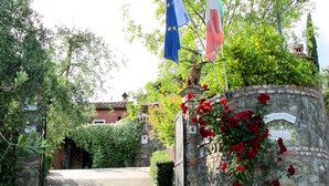 Eine Steinsäule mit einer Gedenktafel, roten Blumen, Flaggen und einem Tor zu einem Gebäude.