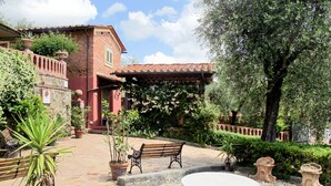 Ein Innenhof mit einem Backsteinhaus, einer Pergola, einer Bank und einem runden Tisch, der von Blumentöpfen und Kies umgeben ist.