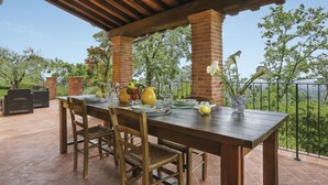 Een terras buiten met een houten eettafel, omringd door bakstenen pilaren en een pergola.