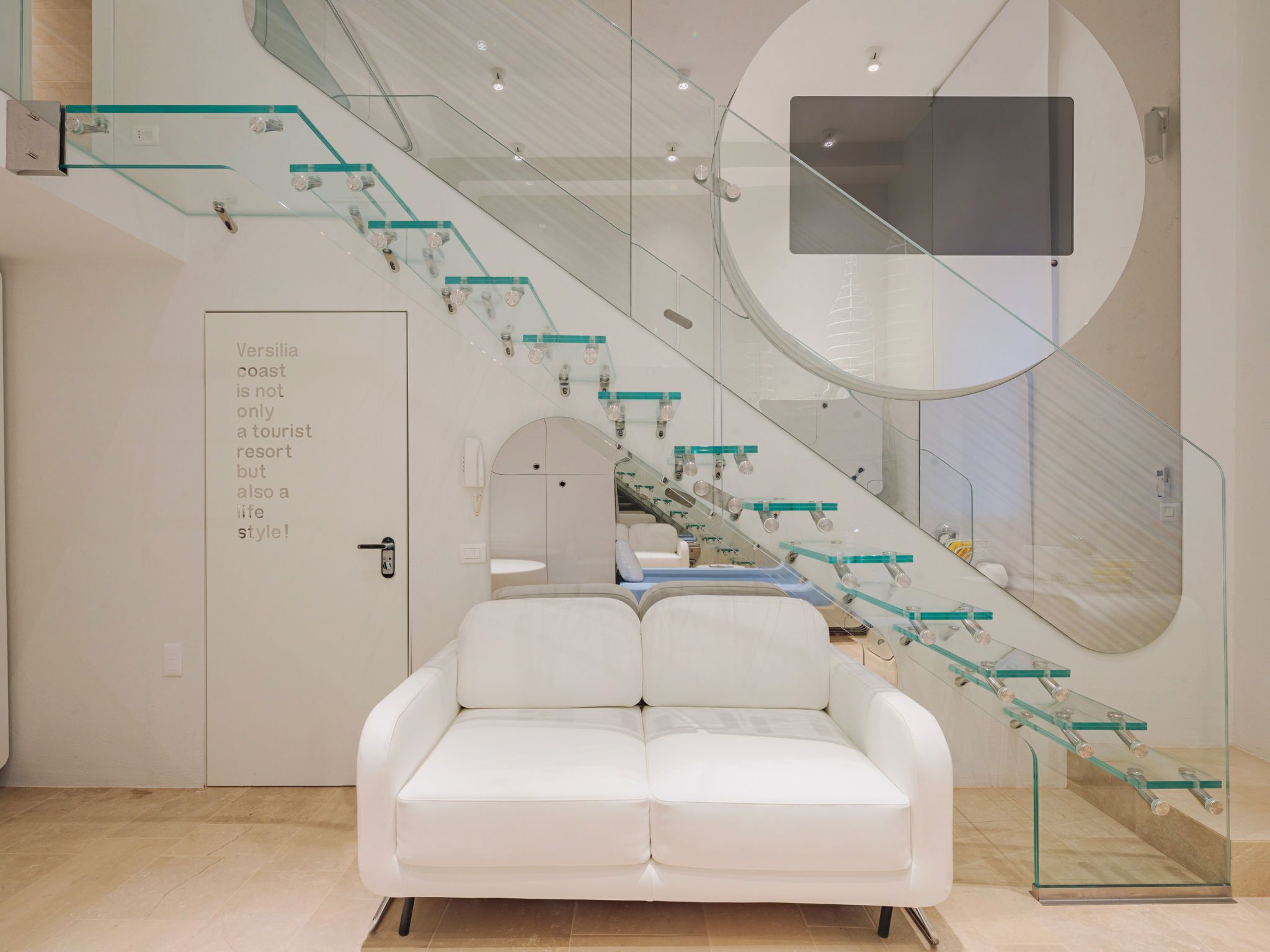 Um interior moderno com uma escada de vidro, um sofá branco e um design minimalista.