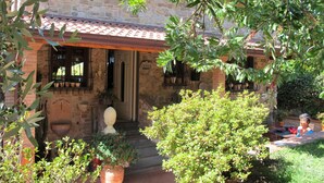 A stone house with a tiled roof, a front porch, and a garden with potted plants. - Capo Corso by Interhome (Corsanico)