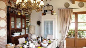 A dining area with a wooden table set for a meal, surrounded by chairs. A chandelier hangs above, and a clock is mounted on the wall. - Capo Corso by Interhome (Corsanico)