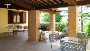 Eine Terrasse im Freien mit Ziegelstützen, einem Grill und Metallstühlen.