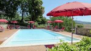 Ein Schwimmbecken mit roten Sonnenschirmen und Liegestühlen.