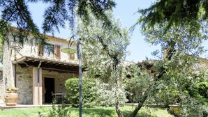 Ein Steinhaus mit einem Ziegeldach, einer Pergola und einem Garten mit verschiedenen Pflanzen und Bäumen.