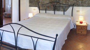 A bedroom with a stone wall, a bed with a metal frame, two bedside tables with lamps, and a wooden nightstand. - Castagno by Interhome (Pastina)