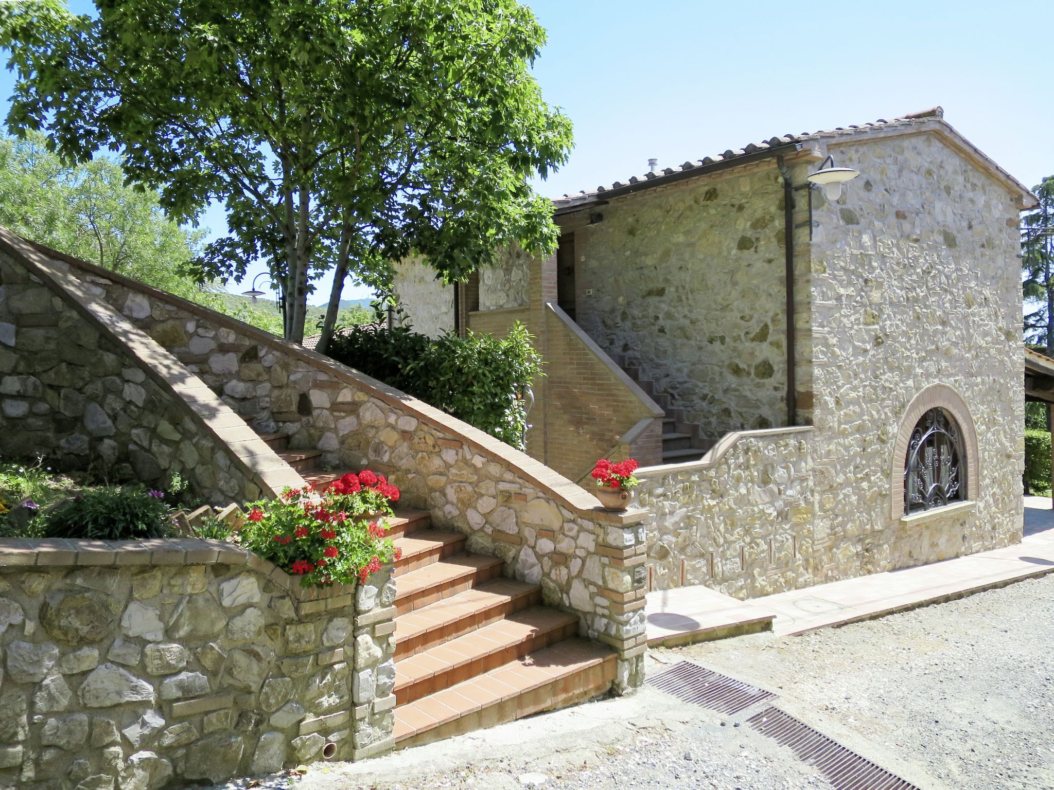 A stone staircase leading to a building with a small arched window and a stone wall with red flowers.
