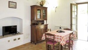 Un coin repas avec une nappe à carreaux, des chaises en bois, un buffet, un téléviseur et une cheminée.