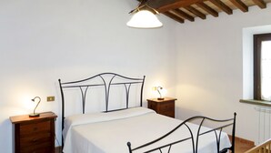 A bedroom with a metal bed frame, two bedside tables with lamps, a wooden dresser, a window with a view, and a wooden staircase. - Apartment Giada by Interhome (Pastina)