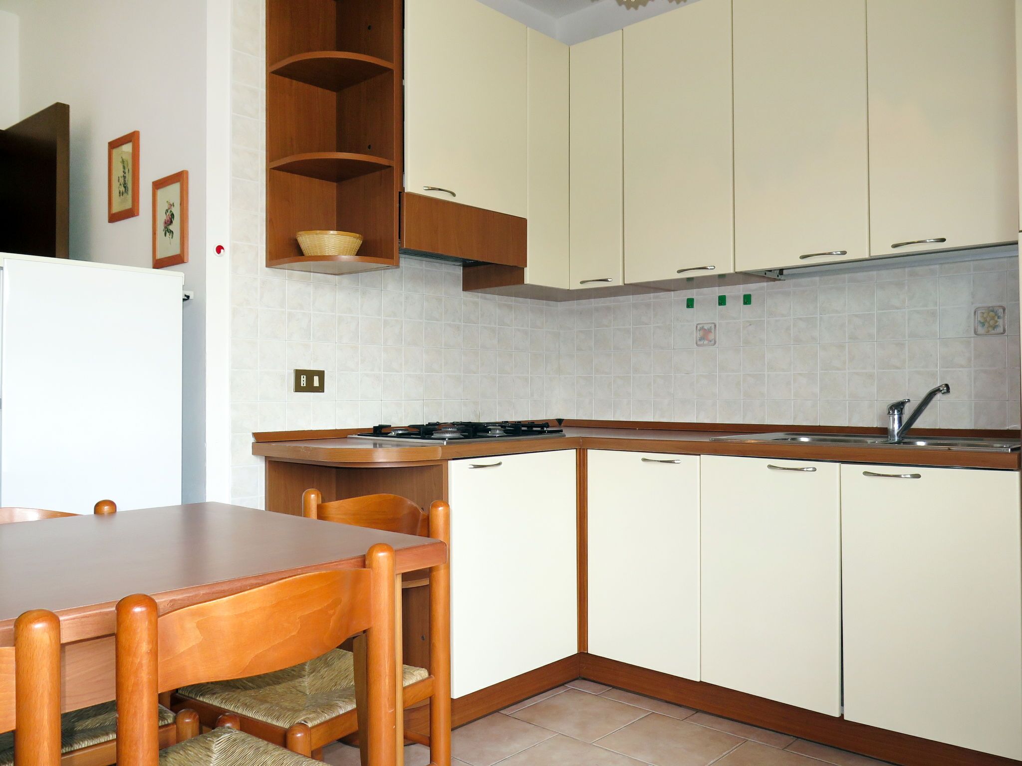 Een keuken met een houten tafel en stoelen, witte kasten en een betegelde achterwand.