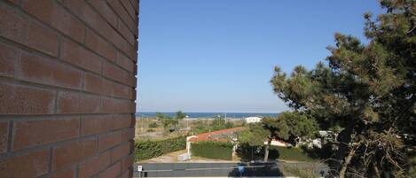 A view from a balcony overlooking a street with a clear blue sky, a parking area, and distant buildings.