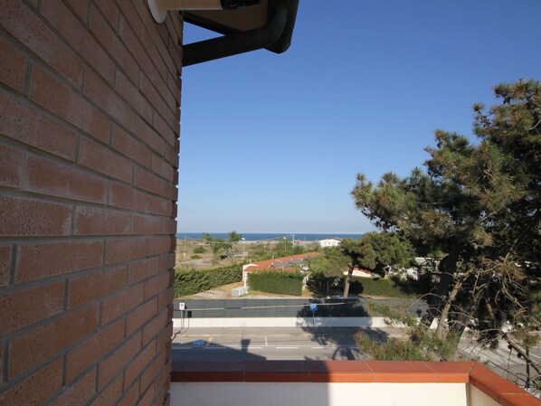 A view from a balcony overlooking a street with a clear blue sky, a parking area, and distant buildings.