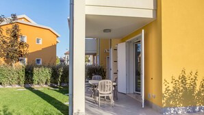 A patio area with a table and chairs, a sliding glass door, and a well-maintained lawn. - Green Village by Interhome (Lido di Jesolo)