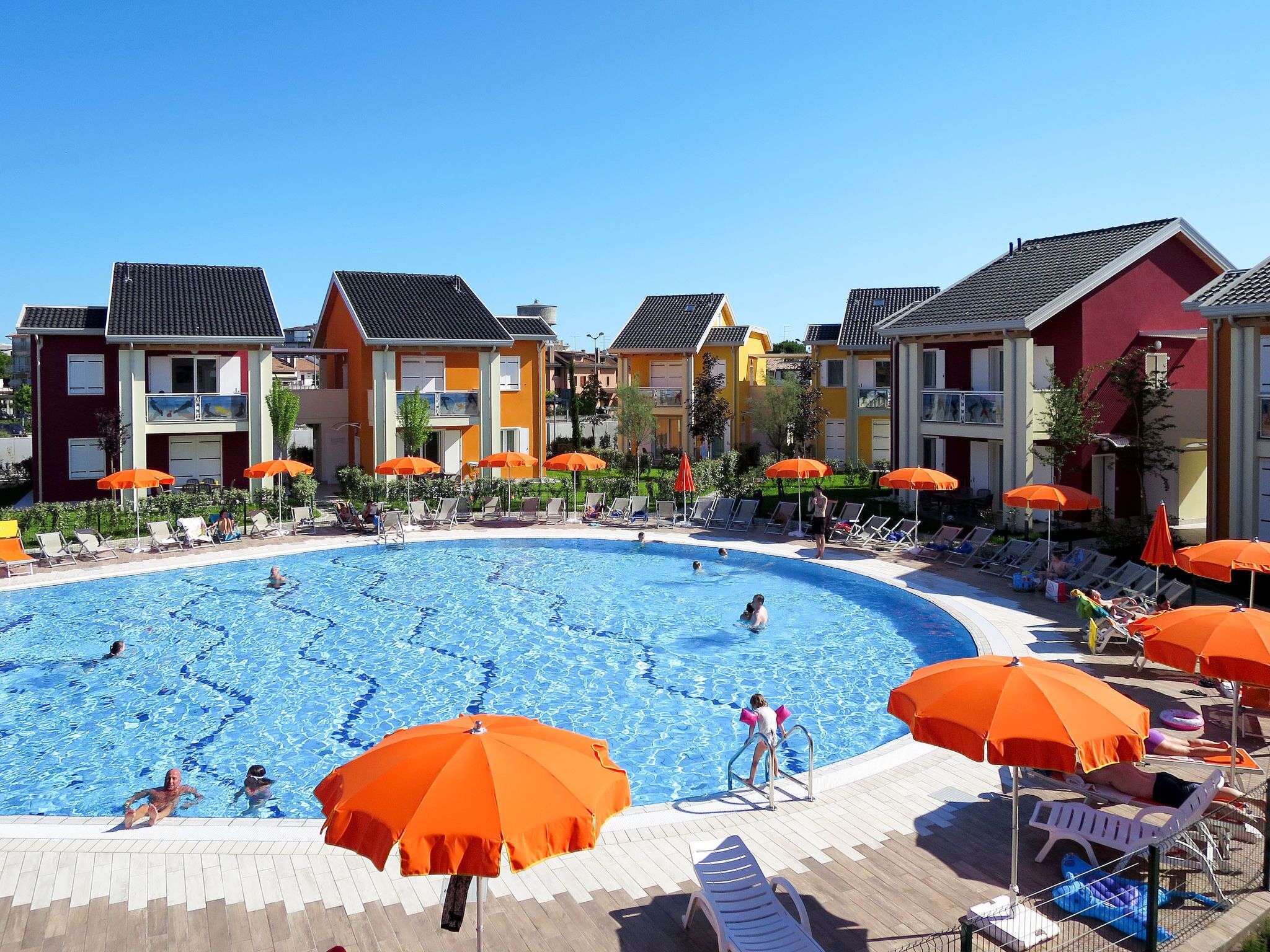 A swimming pool surrounded by colorful buildings with outdoor seating and umbrellas.